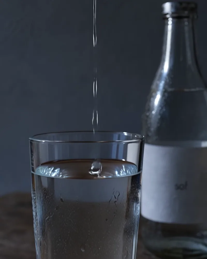 A frame from the film: water from the tap landing in the glass beside the sof bottle